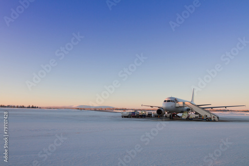 Plane waiting for passangers on a snowy runway in Lapland, Finland. Beautiful sky during sunset photo