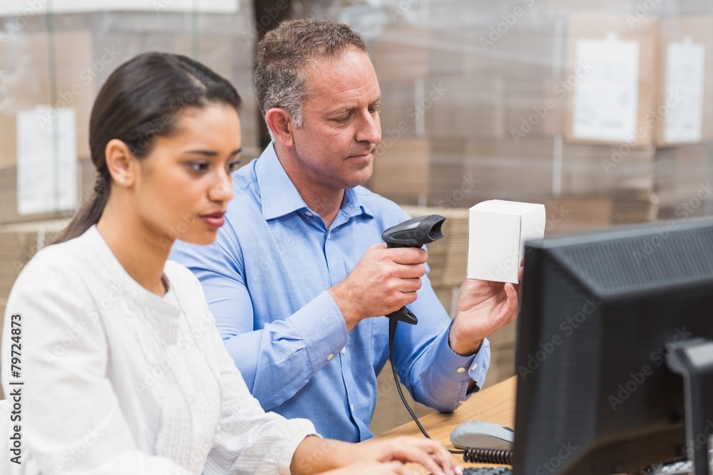 Manager scanning box while his colleague typing on laptop Manager scanning box while his colleague typing on laptop
