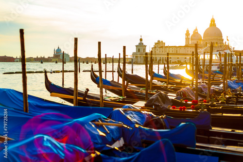 Venetian gondola boats floating on The Grand Canal with The Basilica di Santa Maria della Salute in sunset flare