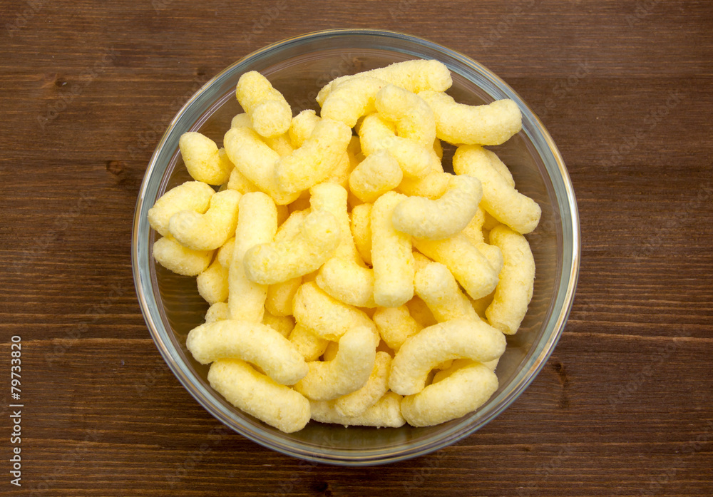 Corn snacks on bowl on wooden table seen from above Corn snacks on bowl on wooden table seen from above