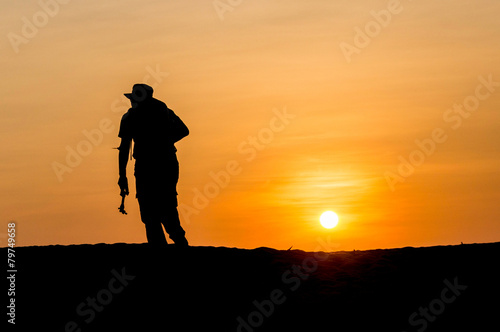 Man in silhouette holding a tripod walking at tropical beach