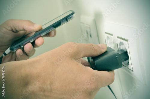 man plugging in the plug of his smpartphone in a socket, with a photo