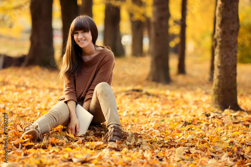 Smiling girl with tablet pc on the autumn landscape, outdoors at