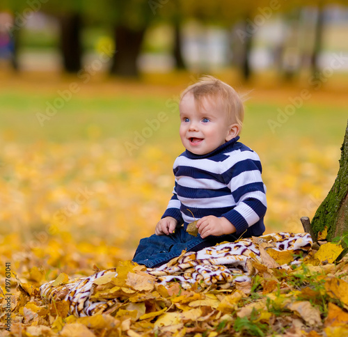 Little boy playing in yellow foliage. Autumn in the city park