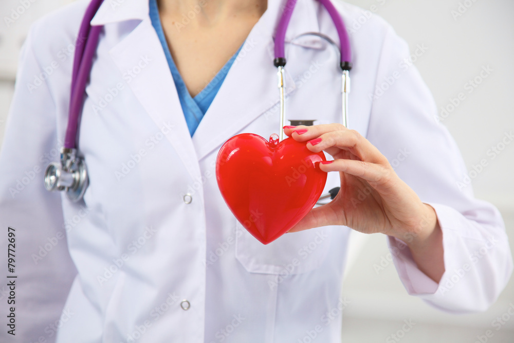Female doctor with stethoscope holding heart over white