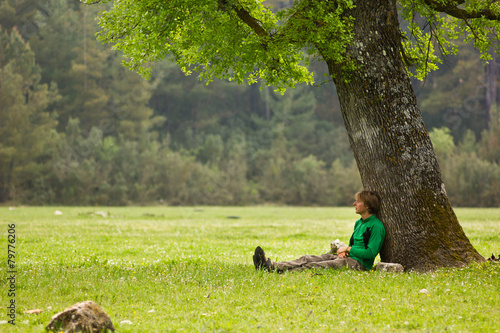 Vászonkép man sitting under big tree on a green meadow