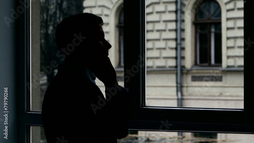 Businessman standing at the window, talking on phone discussing photo