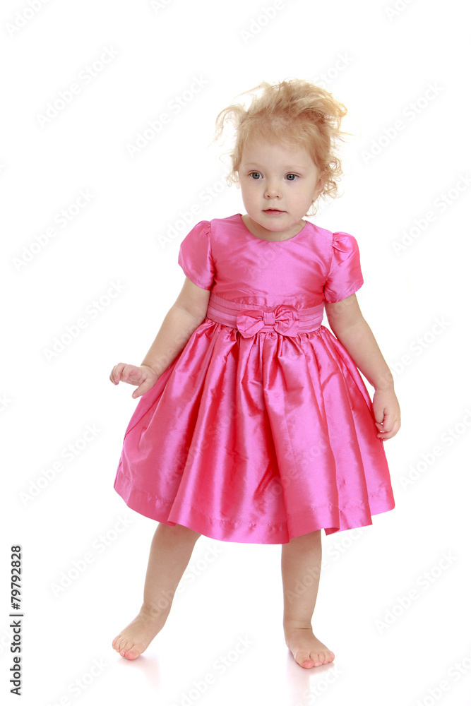 Fashionable little girl in a pink dress standing barefoot