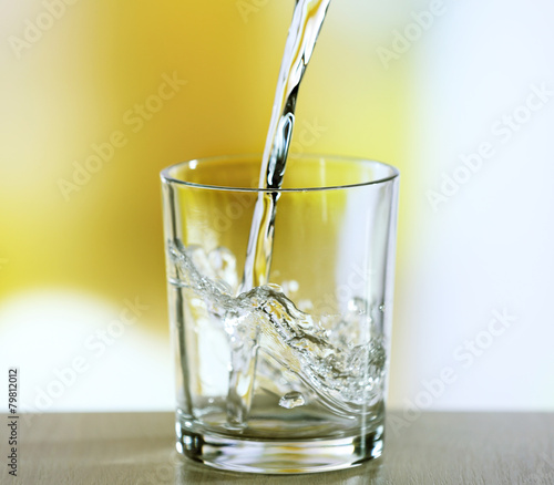 Pouring water from bottle on  glass on light background