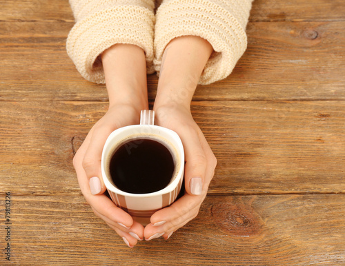 Female hands holding cup of coffee on wooden background