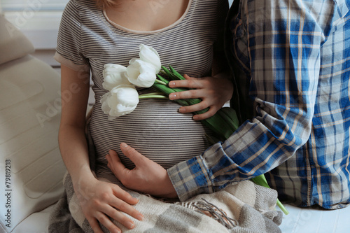 Fototapeta Naklejka Na Ścianę i Meble -  Young pregnant woman sitting with husband and holding flowers