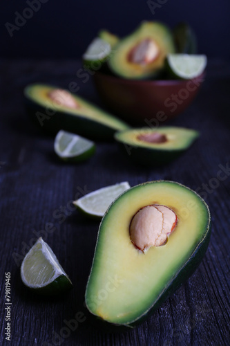 Sliced avocado with pieces of lime on wooden background