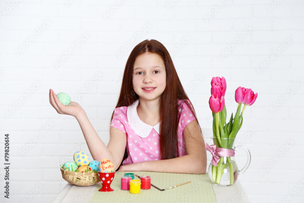 Cute girl decorates Easter eggs, on light background Cute girl decorates Easter eggs, on light background