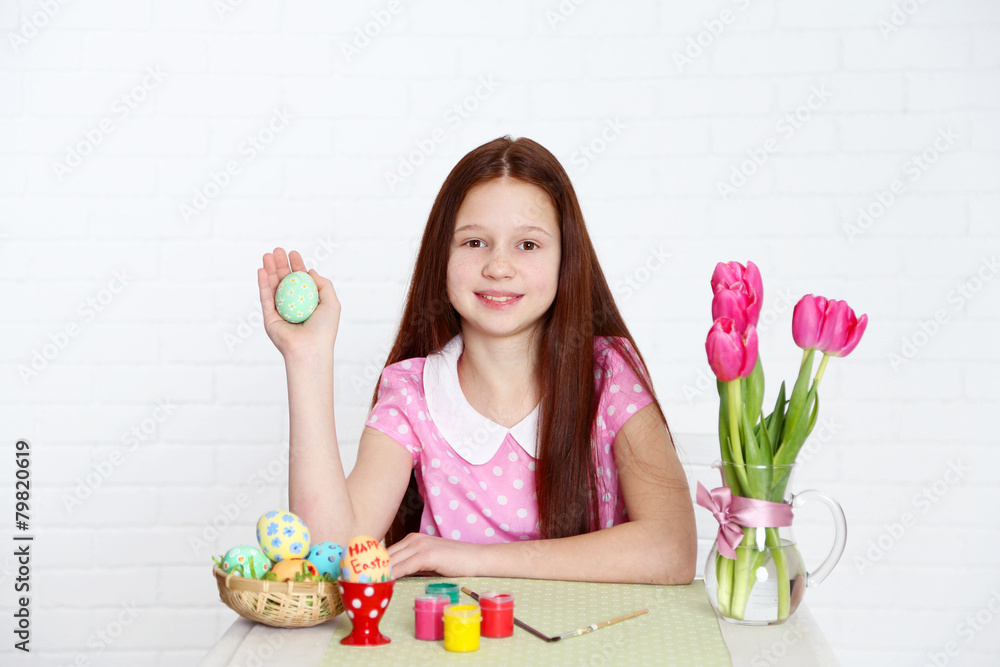 Cute girl decorates Easter eggs, on light background Cute girl decorates Easter eggs, on light background