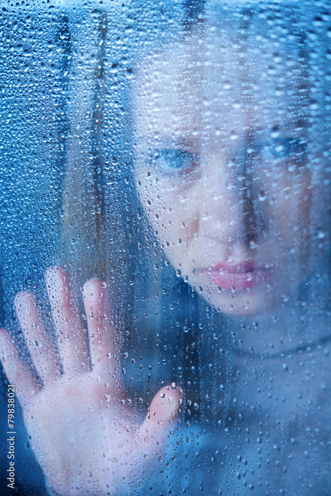 melancholy and sad young  woman  at the window in the rain