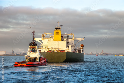 Tanker ship with escorting tug in port.