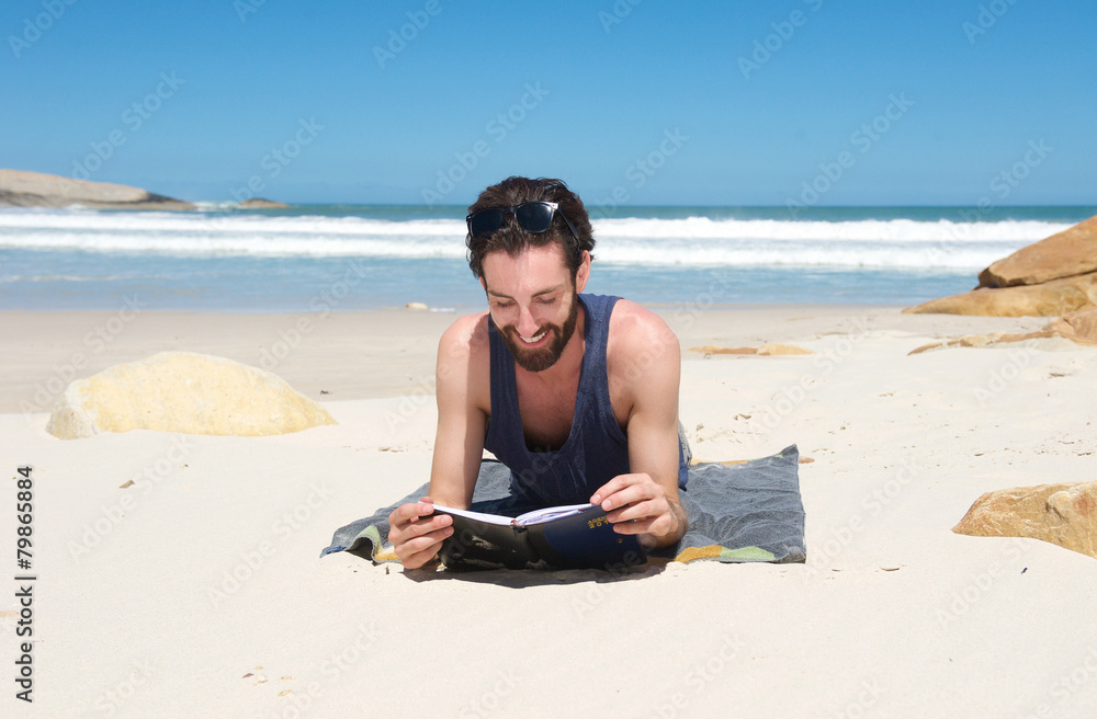 Happy man sitting on the beach reading a book