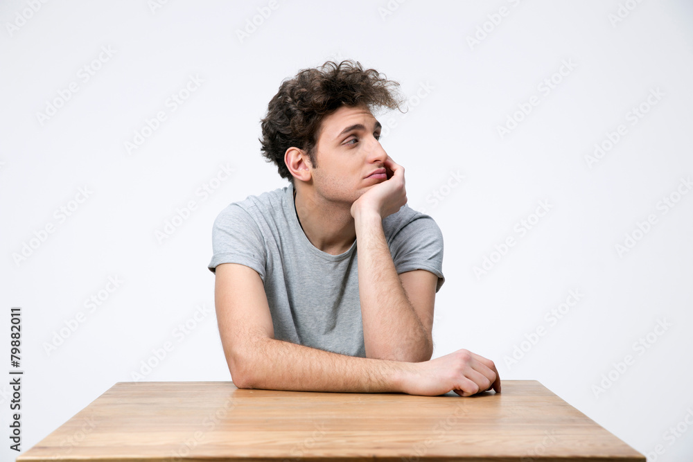 Pensive young man sitting at the table and looking away Pensive young man sitting at the table and looking away