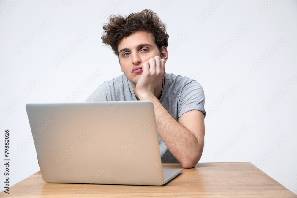 Tired man sitting at the table with laptop over gray background Tired man sitting at the table with laptop over gray background