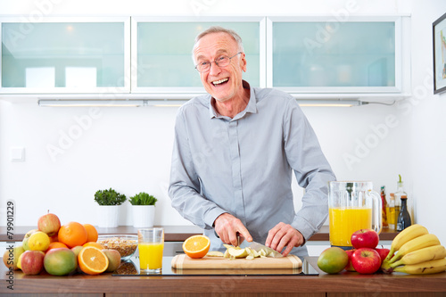 Mature man in the kitchen prepare fruits for breakfast. V