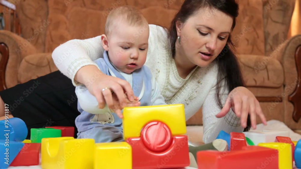 Mother with baby boy playing colored blocks on floor in the room Mother with baby boy playing colored blocks on floor in the room