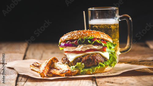 Fresh and juicy hamburger on a paper pad with a beer on a wooden