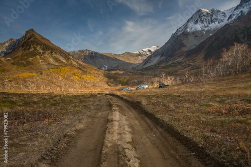 Road to mountain valley. Autumn, first snow. Cars on meadow.