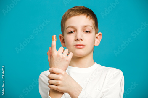 Unhappy boy in white clothes with adhesive plaster on his thumb