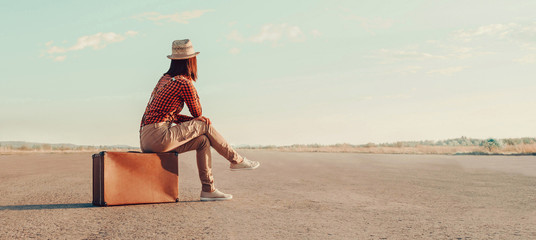 Traveler girl sitting on a suitcase on road