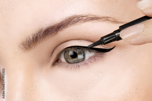 Beautiful model applying eyeliner closeup on eye photo