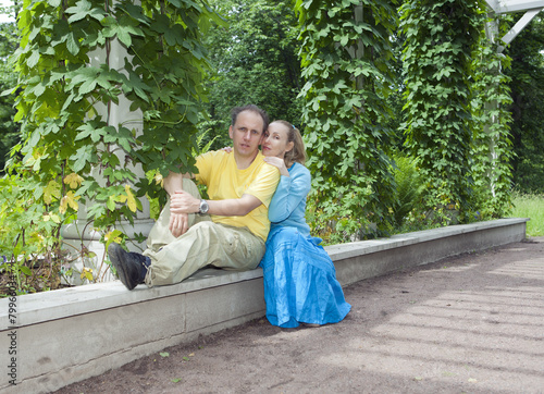 Valokuva Young happy couple sits in the arbour twined greens