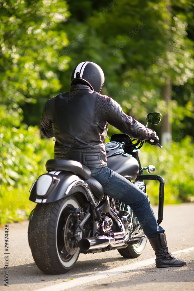 Naklejka premium rowerzysta w masce siedzi nieznany na dużym motocyklu chopper na drodze