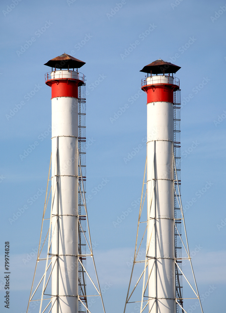 Two high industrial smoke pipes over clear blue sky close up Two high industrial smoke pipes over clear blue sky close up