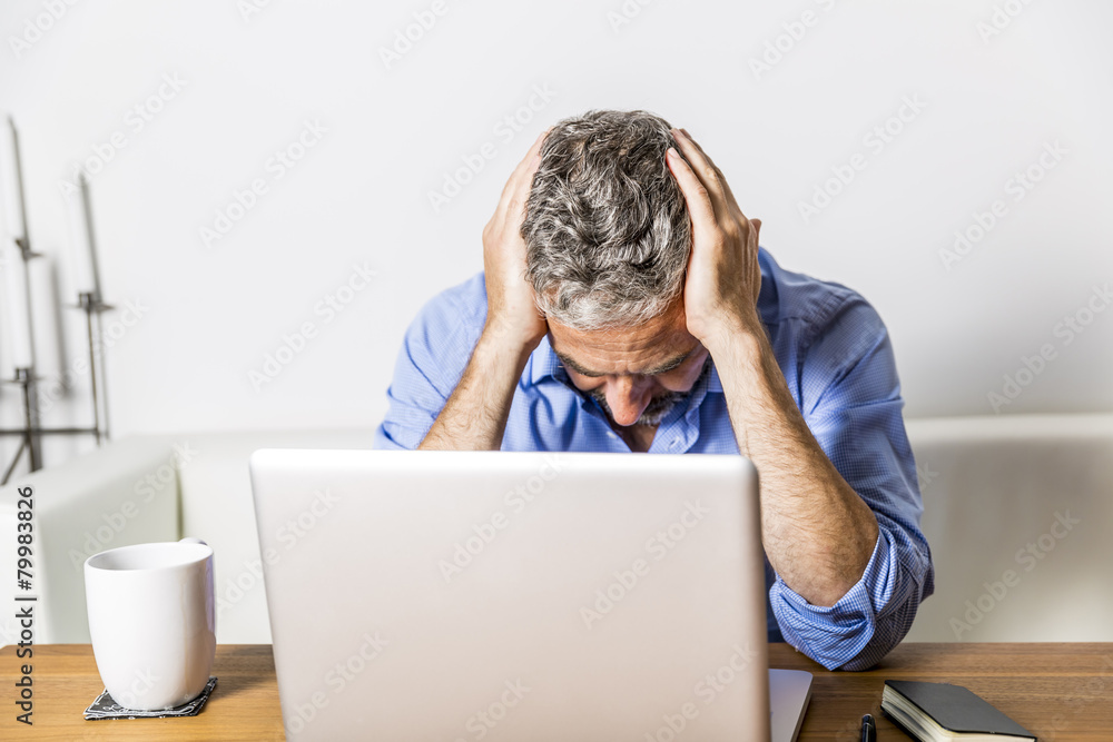 Angry businessman with head in his hands sitting at his home office Angry businessman with head in his hands sitting at his home office