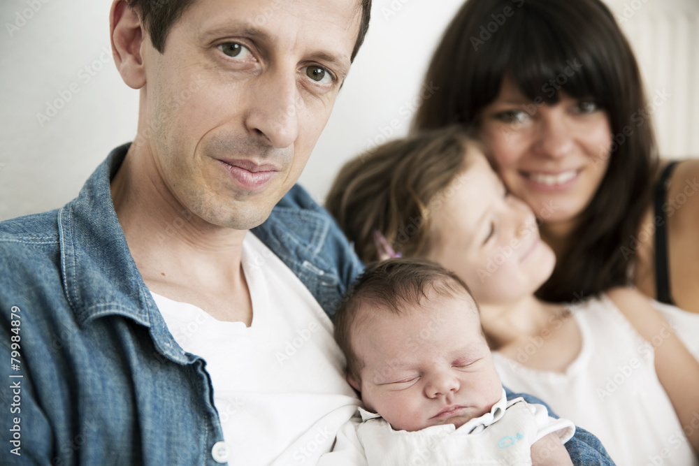 Young parents with male newborn and little daughter sitting on sofa at home Young parents with male newborn and little daughter sitting on sofa at home