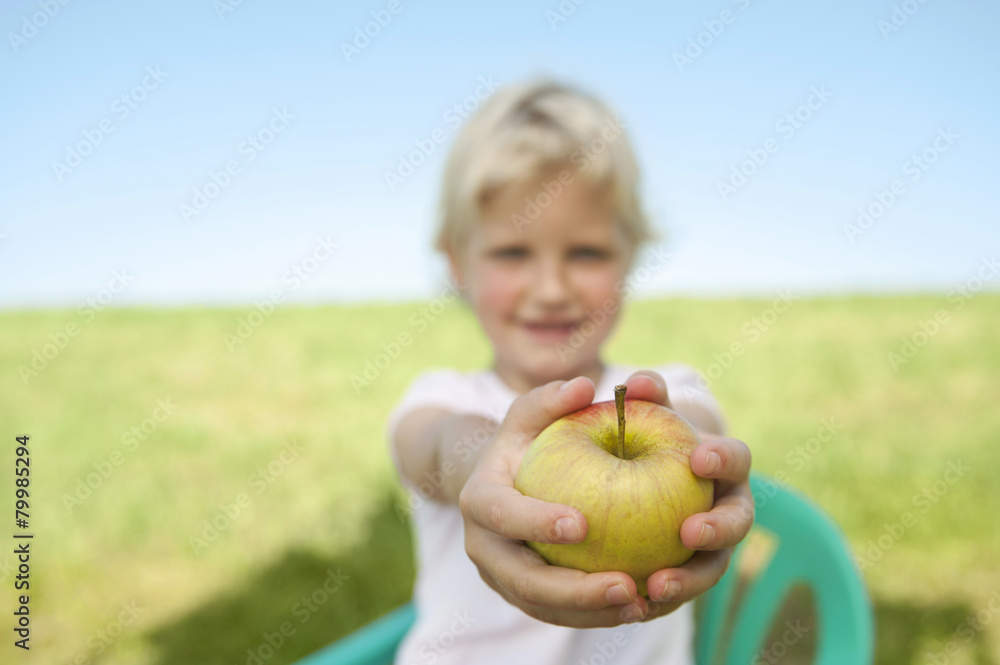 Germany, Bavaria, Girl holding apple fruit in grass meadow, smiling, portrait Germany, Bavaria, Girl holding apple fruit in grass meadow, smiling, portrait