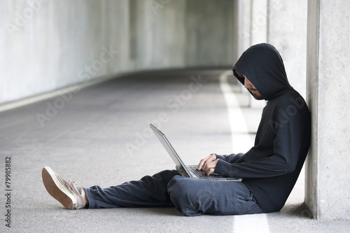 Hacker with laptop sitting in an underground car park photo