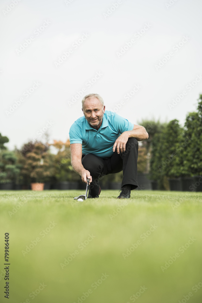 Golf player crouching on turf looking at golf ball Golf player crouching on turf looking at golf ball