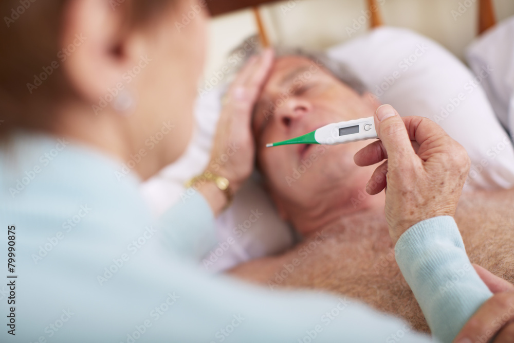 Senior woman taking temperature of sick husband at home Senior woman taking temperature of sick husband at home