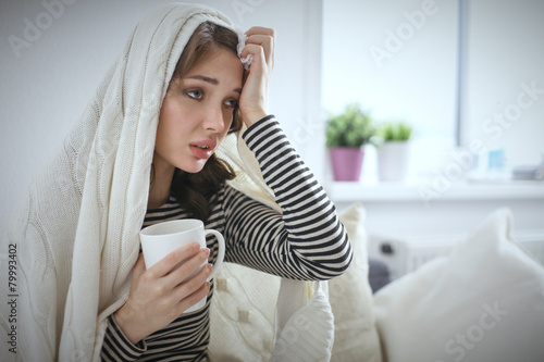 Murais de parede Sick woman covered with blanket holding cup of tea sitting on