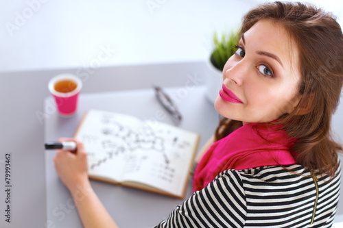 Young woman writes to diary on a white table