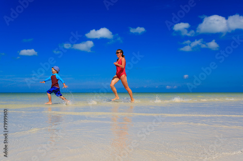 mother and son running in water on summer beach