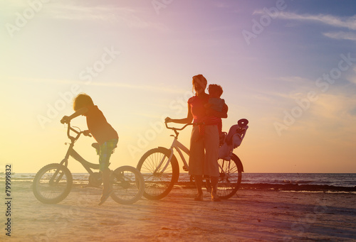 happy mother with kids biking at sunset