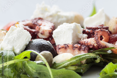 Octopus salad with rucola, olives and feta cheese on white plate