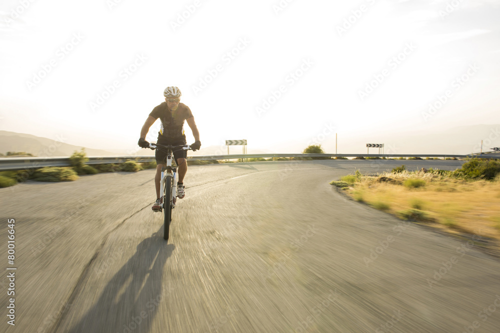 Obraz premium Cyclist man riding mountain bike in sunny day on a mountain road
