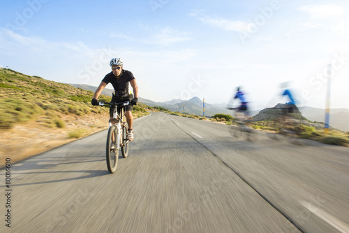 Cyclist man riding mountain bike in sunny day on a mountain road