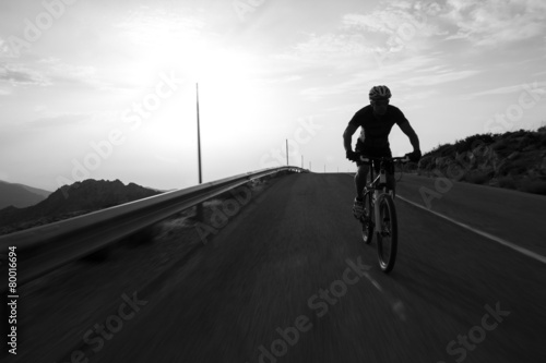 Cyclist man riding mountain on a mountain road, silhouette sunri