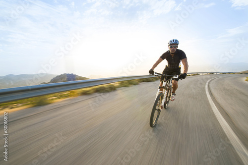 Cyclist man riding mountain bike in sunny day on a mountain road