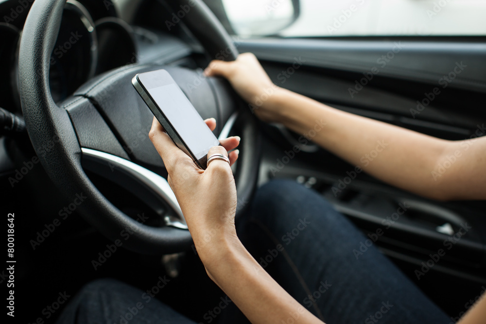 Close-up of a woman hand sending a text while driving, focus on