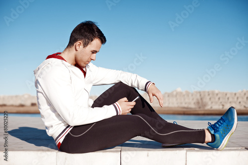 fit athlete sitting outdoors and typing message with smartphone